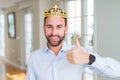 Handsome business man wearing golden crown as a king or prince doing happy thumbs up gesture with hand