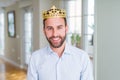 Handsome business man wearing golden crown as a king or prince with a happy and cool smile on face