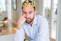 Handsome business man wearing golden crown as a king or prince thinking looking tired and bored with depression problems with