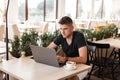 Handsome business young man in a stylish T-shirt with a laptop is sitting in a cafe and typing on a keyboard. Professional blogger