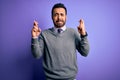 Handsome businessman with beard wearing casual tie standing over purple background gesturing finger crossed smiling with hope and