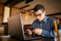Handsome businessman distracted from work on the laptop watching video on smartphone. Freelancer holding mobile phone Royalty Free Stock Photo