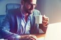 Businessman drinking cup of coffee at table with laptop