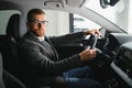 Handsome businessman driving car to airport, going on business side view, copy space. Happy man in stylish suit going to Royalty Free Stock Photo