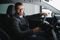 Handsome businessman driving car to airport, going on business side view, copy space. Happy man in stylish suit going to Royalty Free Stock Photo