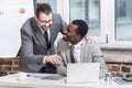 handsome businessman embracing african american partner and pointing at laptop