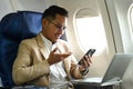 Handsome businessman in formal clothes using mobile phone while sitting in airplane cabin near window