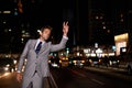 Taxi. A handsome businessman hailing a cab while standing in a busy city street at night. Royalty Free Stock Photo