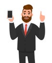 Handsome businessman holding/showing brand new smartphone/mobile/cell phone in hand and pointing index finger upside.
