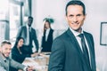 handsome businessman looking at camera in conference hall with multiracial partners blurred