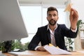 Handsome businessman playing with paper plane at desk in office Royalty Free Stock Photo