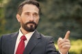 Handsome businessman point to the target in the future. Man in suit and red tie point hand forward over green outside background.