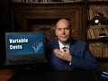 A handsome businessman showing a laptop with sign Variable Costs . Close-up shot. Soft focus