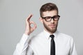 Handsome businessman showing okay sign on gray background.