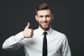 Handsome businessman showing thumbs up sign on dark gray background.