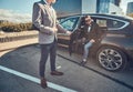 Attractive man in sunglasses is talking by smartphone and sitting in the car while his assistant is opening door for him Royalty Free Stock Photo