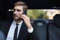 Handsome businessman talking with phone sitting with laptop on the backseat of the car Royalty Free Stock Photo