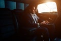 Handsome businessman talking with phone sitting with laptop on backseat of car