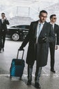 handsome businessman walking with travel bag from car and looking