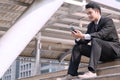 Handsome businessman wearing black suit sitting on stair using smartphone in modern city background. Professional young man Royalty Free Stock Photo