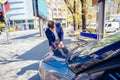A handsome businessman wearing blue blazer lifting up the hood of his car and checking the oil level on a sunny day parked on a