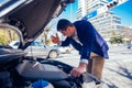 A handsome businessman wearing blue blazer lifting up the hood of his car and checking the oil level on a sunny day parked on a