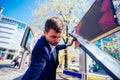 A handsome businessman wearing blue blazer lifting up the hood of his car and checking the oil level on a sunny day parked on a