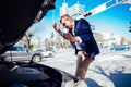 A handsome businessman wearing blue blazer lifting up the hood of his car and checking the oil level on a sunny day parked on a