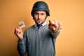 Handsome businessman wearing military helmet holding reminder paper with war message pointing with finger to the camera and to