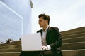 Handsome businessman wearing suit and using modern laptop outdoors. Successful banker working outside during break. Royalty Free Stock Photo