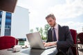Handsome businessman wearing suit and using modern laptop outdoors, successful manager working in cafe during break and Royalty Free Stock Photo