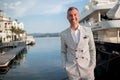 Handsome businessman is wearing white fashion costume stands on the background of the bay with luxury yachts. Montenegro Royalty Free Stock Photo