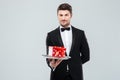 Handsome butler in tuxedo with bowtie gift box on tray