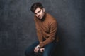 Handsome casual man sits on chair near a dark gray wall and looks to side, portrait picture. Royalty Free Stock Photo