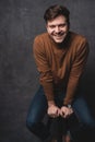 Handsome casual man sits on chair near a dark gray wall and looks to side, portrait picture. Royalty Free Stock Photo