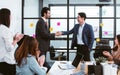 Handsome Caucasian and Asian businesspeople and partners doing hand shaking to deal business agreement while colleagues applause