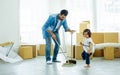 Handsome Caucasian father using broom sweep floor in living room at home or apartment, taking care daughter. Little naughty girl