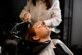 handsome female client relaxed lying on hair washing chair with her eyes closed while hairdresser washes her hair Royalty Free Stock Photo