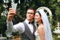 Handsome caucasian groom and beautiful asian bride doing self portrait from cell phone with happy smiling face during wedding or Royalty Free Stock Photo