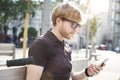 Handsome caucasian hipster man using mobile phone sitting outdoor in a park. Summer sunshine day. Concept of young business people