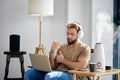 bearded caucasian male sit working on laptop, with purifier in room, in smart house