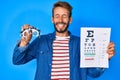 Handsome caucasian man with beard holding optometry glasses and eyesight test smiling and laughing hard out loud because funny Royalty Free Stock Photo