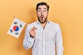 Handsome caucasian man with beard holding south korea flag scared and amazed with open mouth for surprise, disbelief face Royalty Free Stock Photo