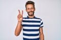 Handsome caucasian man with beard wearing casual striped t-shirt smiling with happy face winking at the camera doing victory sign Royalty Free Stock Photo