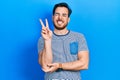 Handsome caucasian man with beard wearing casual striped t shirt smiling with happy face winking at the camera doing victory sign Royalty Free Stock Photo