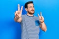 Handsome caucasian man with beard wearing casual striped t shirt smiling looking to the camera showing fingers doing victory sign Royalty Free Stock Photo