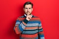 Handsome caucasian man with beard wearing elegant wool winter sweater asking to be quiet with finger on lips