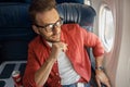 Handsome caucasian man in casual wear and glasses looking thoughtful, sitting on the plane near the window Royalty Free Stock Photo
