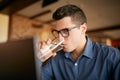 Handsome caucasian man with glass of water in hand works with laptop. Businessman in glasses drinks water for body