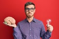 Handsome caucasian man holding brain and lightbulb for inspiration and idea puffing cheeks with funny face